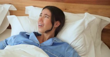 Mavi pijamalı bir kadın yatakta uyanıyor, esniyor ve esniyor, evde. Sabah, uyanma, rahatlama, konfor, konfor, yaşam tarzı