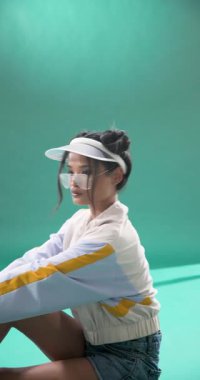 Dikey video: Şık şapkalı ve ceketli genç kadın stüdyoda güven içinde poz veriyor. Moda, kentsel, modern, trend, güven, tarz