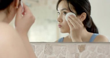 Asyalı kadın banyo lavabosundaki soğuk musluğun altında durulanıyor makyajı silmek için yüzünü siliyor, gülümsüyor. Güzellik, cilt bakımı, hijyen, yansıma, günlük rutin, minimalist, sağlıklı.