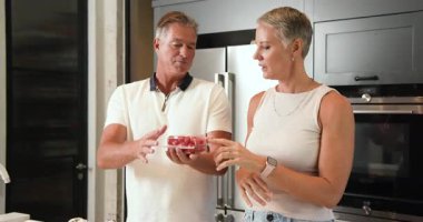 Mutfakta erzak tartışan, kavanozu tutan ve el kol hareketi yapan olgun bir çift. Yaşlılar, evcil hayat, sohbet, ev, beslenme