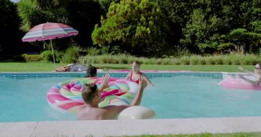 Çeşitli arkadaşlar geri sayım yapıyor arka bahçedeki havuza atlıyorlar yüzme havuzuna su sıçratıyorlar ve eğlence için yüzüyorlar. Eğlence, eğlence, yaz, su oyunu, arkadaşlık, açık hava, canlı