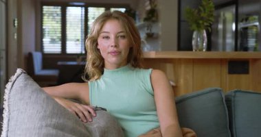 Evdeki gri kanepede uzanan kadın yastığı tutuyor, gülümsüyor, kamera dışı çağrıya cevap veriyor. Rahatlama, rahatlık, modern ev, dinginlik, yaşam tarzı, minimalizm