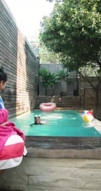 Dikey video: Anne ve kızı havuz başında rahatlamanın keyfini çıkarıyor, birlikte neşeli gülümsemeler paylaşıyorlar. Aile, birliktelik, eğlence, bağlanma, mutluluk, tatil