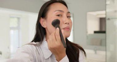 Smiling at camera Asian woman grabbing brush, applying blush and eyeshadow at vanity for tutorial. Beauty, skincare, makeup, elegance, self-care, lifestyle, natural light