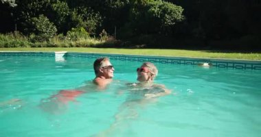 Olgun bir çift sabah havuzda yüzüyor, gülümsüyor ve güneş gözlüğü takıyor. Boş zaman, dinlenme, tatil, yaşlı çift, yaşam tarzı, yüzme.