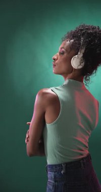 Dikey video: Kulaklık takan, şık stüdyo ortamında neşeyle dans eden kadın. Dans, müzik, coşku, hareket, moda, ifade