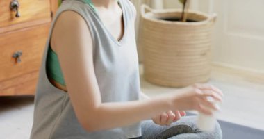 Asyalı kadın antrenmanı bitiriyor. Suyla takviye alıyor. Oturma odasında akıllı saatleri kontrol ediyor. Farkındalık, sağlık, canlılık, rahatlama, modern yaşam tarzı, sağlık