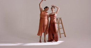 Çeşitli kadın modeller omuz omuza dinleniyor ve stüdyo merdivenlerinde paslı elbiseleri gösteriyor. Sanatçılık, zarafet, uyum, dans, hareket, moda, minimalist