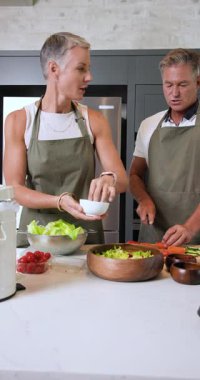 Dikey video: Mutfakta, olgun çift taze salata hazırlıyor, sohbet ediyorlar. Aşçılık, yaşam tarzı, aşçılık, sağlıklı beslenme, sebze, arkadaşlık.