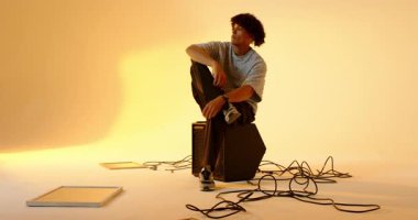 Adam hoparlör kutusunda çenesini dinlendiriyor sonra da kehribar ışıklı stüdyoda çekim için el kol hareketi yapıyor. Düşünce, stüdyo, modern, profesyonel, minimalist, sanatsal, rahat