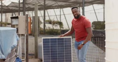 Kırmızı gömlekli bir adam sürdürülebilir serada güneş panelini inceliyor. Sürdürülebilirlik, çevre, yeşil enerji, yenilenebilir, denetim, teknoloji