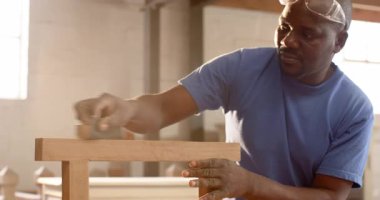 Afrika kökenli Amerikalı bir adam kum bloğunu kavrıyor, atölye ışığında çerçeveyi düzleştiriyor, tozu inceliyor. Sanatçılık, marangozluk, esnaf, manüel, yenileme, beceri, çalışma alanı
