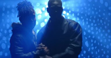 Farklı arkadaşlar mavi ışıklı stüdyoya çıkıyorlar, LED panelinde el ele tutuşuyorlar, birlikte dönüyorlar. Bağlantı, işbirliği, birlik, dinamik, modern, atmosferik, performans