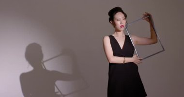 Stüdyoya giren Asyalı Çinli kadın sahne ışıkları altında kare çerçeveyi manipüle ederek siluet yaratıyor. Minimalist, siluet, performans, monokrom, sanatsal, dinamik, zarafet