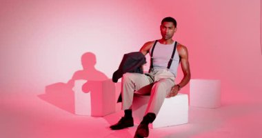 Ceket tutan Afro-Amerikalı bir adam stüdyoda oturup kol saatini kontrol ediyor. Moda, minimalist, kendinden emin, tarz, profesyonel, modern, kentsel