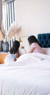 Dikey video: Anne ve kızı yatakta dinleniyor, akıllı telefonla selfie çekiyor, mutlu bir şekilde gülümsüyor. Aile, bağ, yaşam tarzı, birliktelik, teknoloji, portre