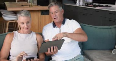 Evde tablet ve akıllı telefon kullanan olgun bir çift planlarını tartışıyor. Teknoloji, planlama, iletişim, yaşam tarzı, dijital, kıdemli