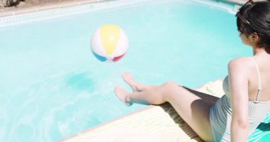 Telefonları dinlemek, plaj topunun zıpladığını fark etmek, oynamak için havuza dalan Asyalı bir kadın, kopyalama alanı. Tatil yeri, boş zaman, hayat tarzı, rahatlama, açık hava, oyuncu.