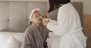 Çinli anne ve kız, yatak odasında maske takan ve göz altı bantları takan kız. Cilt bakımı, refah, şımartma, rahatlama, güzellik, samimiyet, özgüven.