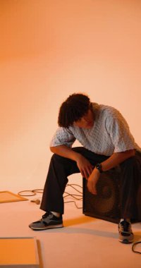 Dikey video: Genç adam hoparlörde oturuyor, yaratıcı stüdyo ortamını düşünüyor. müzik, müzisyen, düşünceli, ilham, ses, sanatsal