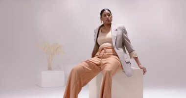 Stüdyodaki kurutulmuş sazlıklar tarafından öne doğru eğilip beyaz küpün üzerinde kıvrılan Hintli kadın. Stüdyo, minimalizm, zarafet, esneklik, sağlık, meditasyon, moda