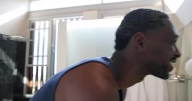 Afrikalı Amerikalı adam modern banyodaki yansımayı kontrol ediyor, yuvarlak lamba armatürlerinin yanında. Bakım, yansıma, modern, parlak, sağIık, kendine dikkat, doğal ışık.