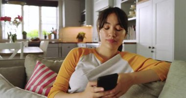 Mesaj uyarısı Asyalı kadınların açık planlı oturma odasındaki koltukta akıllı telefonları dinlemesine ve kaydırmasına neden oluyor. Rahatlama, yaşam tarzı, modern, rahat, iletişim, eğlence, teknoloji