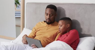 Tableti izlemek için ayarlamak, Afrikalı Amerikalı baba ve oğulun yatak paylaşma hikayesinde sayfa okutması. Aile, bağ, teknoloji, uyku zamanı, eğitim, şefkat, konfor