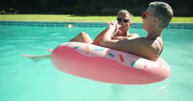 Bilardoda yürüyen, mayo giyen, arka bahçedeki havuzda dönen pembe donut yüzüğü takan bir çift dinlenmeyi kutluyor. Boş zaman, yaz, rahatlama, dostluk, şakacı, açık hava, canlı
