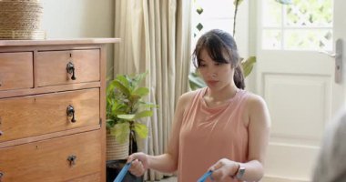 Asyalı kadın tablet antrenmanını takip ediyor bandı çekiyor ve evdeki gelişmeleri takip ediyor. Fitness, kuvvet, esneklik, farkındalık, sağlık, spor, spor