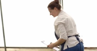 Önlüklü kadın panoya yazı yazıyor, seradaki işine odaklanıyor. Bahçıvanlık, bahçıvanlık, tarım, tarım, tarım, bitkiler, botanikçi.