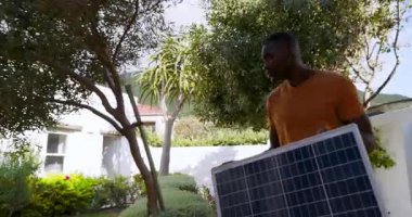 Bahçedeki adam güneş paneli tutuyor güneşli günün ve sürdürülebilir yaşamın tadını çıkarıyor. Yenilenebilir enerji, çevre dostu, bahçıvanlık, teknoloji, çevre