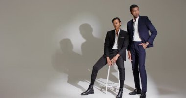 Diverse male models receiving spotlight stepping on stool and adjusting suits in studio for shoot. Fashion, elegance, professionalism, studio, monochrome, contrast, lighting