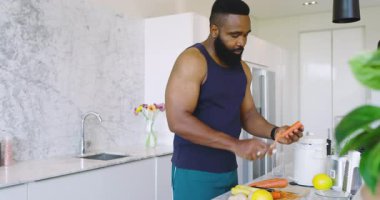 Modern mutfakta sebze ve akıllı telefonla havuç soyan Afro-Amerikalı bir adam. Yemek, sebze, hazırlık, gurme, modern, sağlıklı, canlı