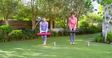Asian Chinese instructor and senior student crossing garden lawn with mats bottles warming up. Fitness, wellness, outdoor, serenity, balance, harmony, mindfulness
