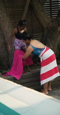 Dikey video: Anne ve kızı renkli havlulara sarılı havuz başında eğleniyorlar. Aile, kaynaşma, boş zaman, yaz, rahatlama, su