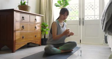 Şişeden tablet toplayan Asyalı kadın, su içen, akıllı adam kontrol eden, paspas üzerinde meditasyon yapan. Sağlık, farkındalık, fitness, rahatlama, uyum, iç mekan, yaşam tarzı