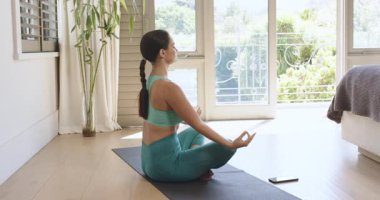 Eve gelen kadın paspasın üzerinde oturuyor kollarını kaldırıyor Mudra telefonuna nefes veriyor, kopyalama uzayı. Sağlık, farkındalık, dinginlik, disiplin, modern, içsel, sağlıklı