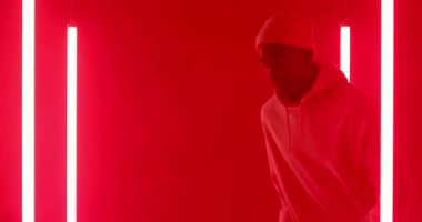 Afro-Amerikalı bir adam hayali işaretleri fark ediyor, ayağa kalkıyor, kırmızı stüdyoda neon tüplerle dans ediyor. Performans, koreografi, dans, neon, minimalist, stüdyo, ifade