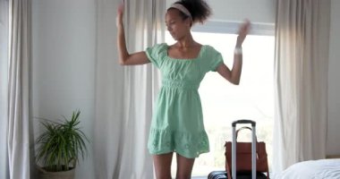 Yeşil elbiseli kadın evde bavuluyla neşeyle dans ediyor. seyahat, mutluluk, özgürlük, yaşam tarzı, kapalı alan, boş zaman