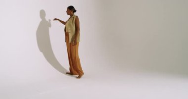 Stüdyo duvarına doğru yürüyen Hintli kadın içeri giriyor. Gölge ve modelleme, kopyalama alanı. Minimalist, zarif, hareketli, moda, siluet, çağdaş, sanatsal