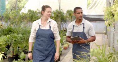 Bahçe merkezi çeşitli işçiler, bitki stoklarını yönetmek için tablet, serada detayları tartışmak. Bahçe işleri, takım çalışması, teknoloji, işbirliği, bahçıvanlık, yönetim