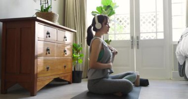 Kulaklıklar çalıyor, Asyalı bir kadın şişeyi ve battaniyeyi yerleştiriyor, evde nefes alıp veriyor, fotokopi çekiyor. Sağlık, farkındalık, sükunet, rahatlama, fitness, meditasyon, iç mekan.