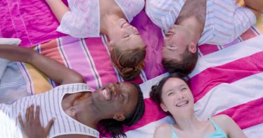 Çeşitli arkadaşlar parkta çizgili battaniyeye uzanmış başlarının üstünde hareket fark ediyor, işaret ediyor, sohbet ediyorlar. Rahatlama, yoldaşlık, açık hava, eğlence, canlı, yeniden bağlanma, hikaye anlatma.