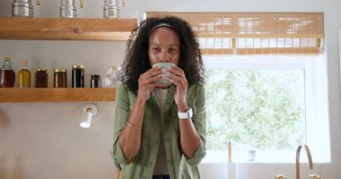 Gülümseyen kadın evde kahveden zevk alıyor, şık giyiniyor, rahatlıyor. Yaşam tarzı, rahatlama, teknoloji, sabah, rahat, içecek