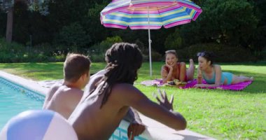 Çeşitli arkadaşlar akıllı telefon kliplerini paylaşıyorlar, plaj topu atıyorlar, şemsiye altında üzümleri bilardo oynuyorlar. Eğlence, eğlence, açık hava, hayat, yaşam tarzı, arkadaşlık, yaz mevsimi.