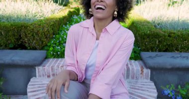 Kamera, açık hava yaşam tarzı çekimi sırasında bahçe bankında gülümseyen orta yaşlı bir kadın olduğunu gösteriyor. Doğa, sağlık, rahatlık, zarafet, sükunet, moda, açık hava