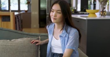 Kameraya dikkat, Asyalı bir kadının koltukta duruşunu değiştirmesi, başını çevirmesi, gülümsemesi diş tellerini ortaya çıkarması. Rahatlama, samimi, rahat, iç mekan, doğal ışık, çağdaş, dostane