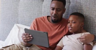Afrika kökenli Amerikalı baba ve oğul oturma odasında gri koltukta oturup tablet hikayesini izleyip tepki veriyorlar. Aile, bağ, eğitim, teknoloji, rahat, duygusal, akıl hocalığı