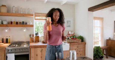 Kadın mutfakta taze meyve suyu dolduruyor, gülümsüyor ve sabah evde eğleniyor. Kahvaltı, yaşam tarzı, sağlık, beslenme, ev, mutluluk.